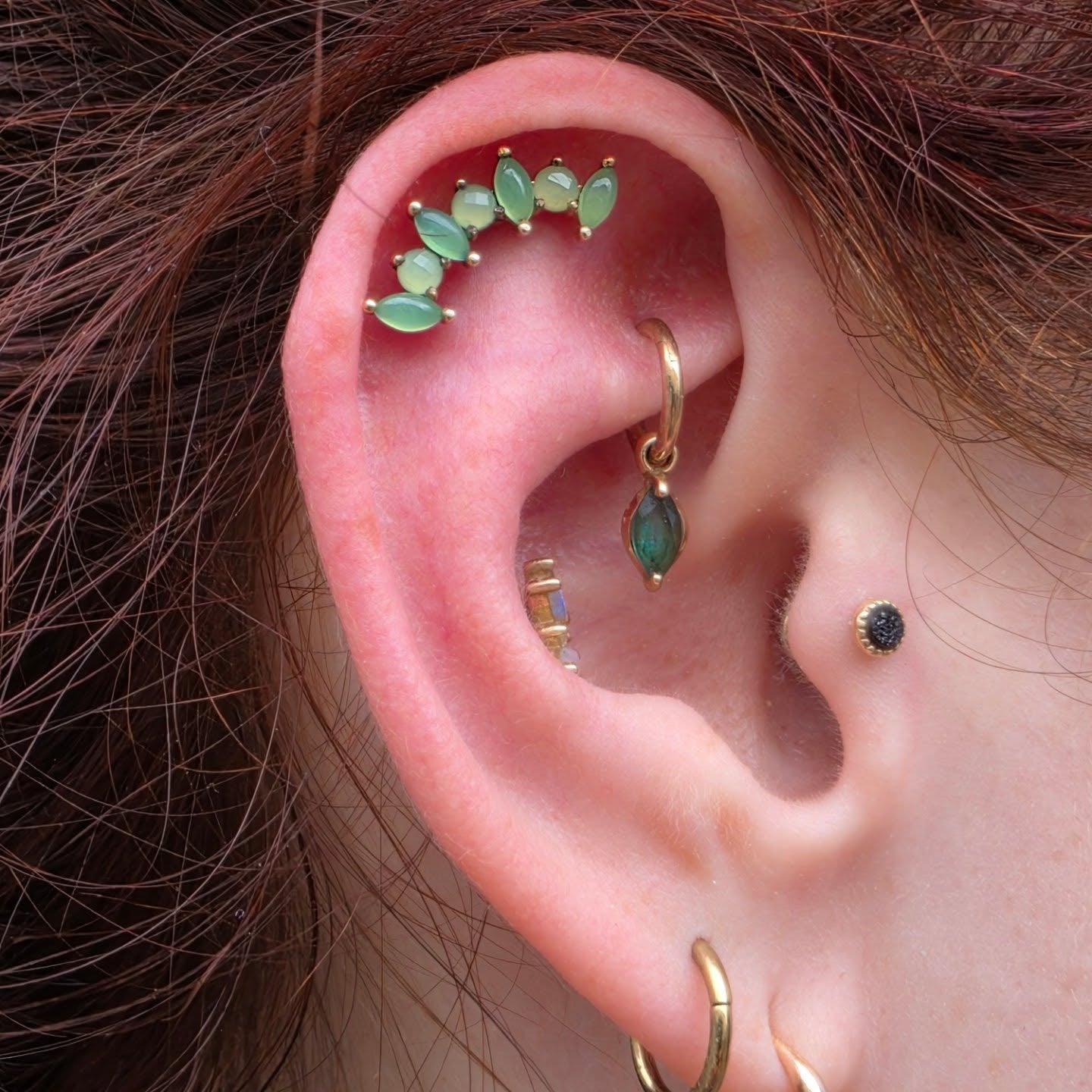 photo d'une oreille avec un piercing a l'helix, un au daith, un au conch et un au tragus, avec des bijoux de piercing en or jaune 4k et chrysoprases, bijoux disponibles chez kawaii place a lille